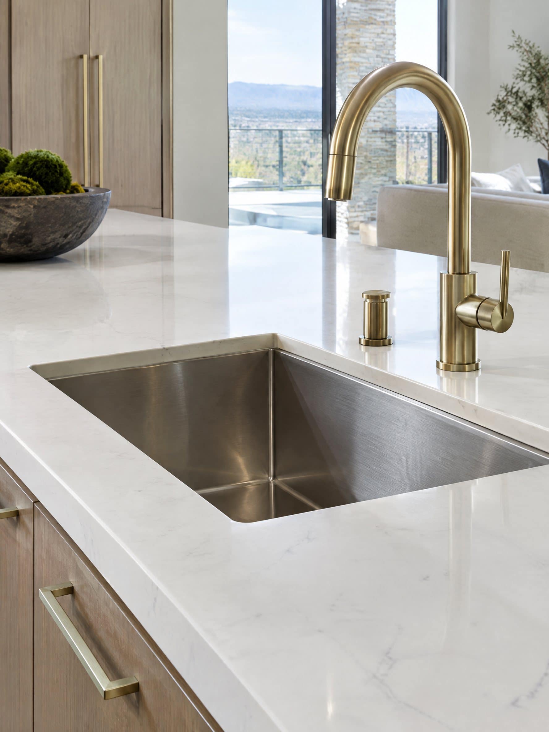 White engineered quartz kitchen counter with an eased edge, undermount stainless sink and brushed brass faucet