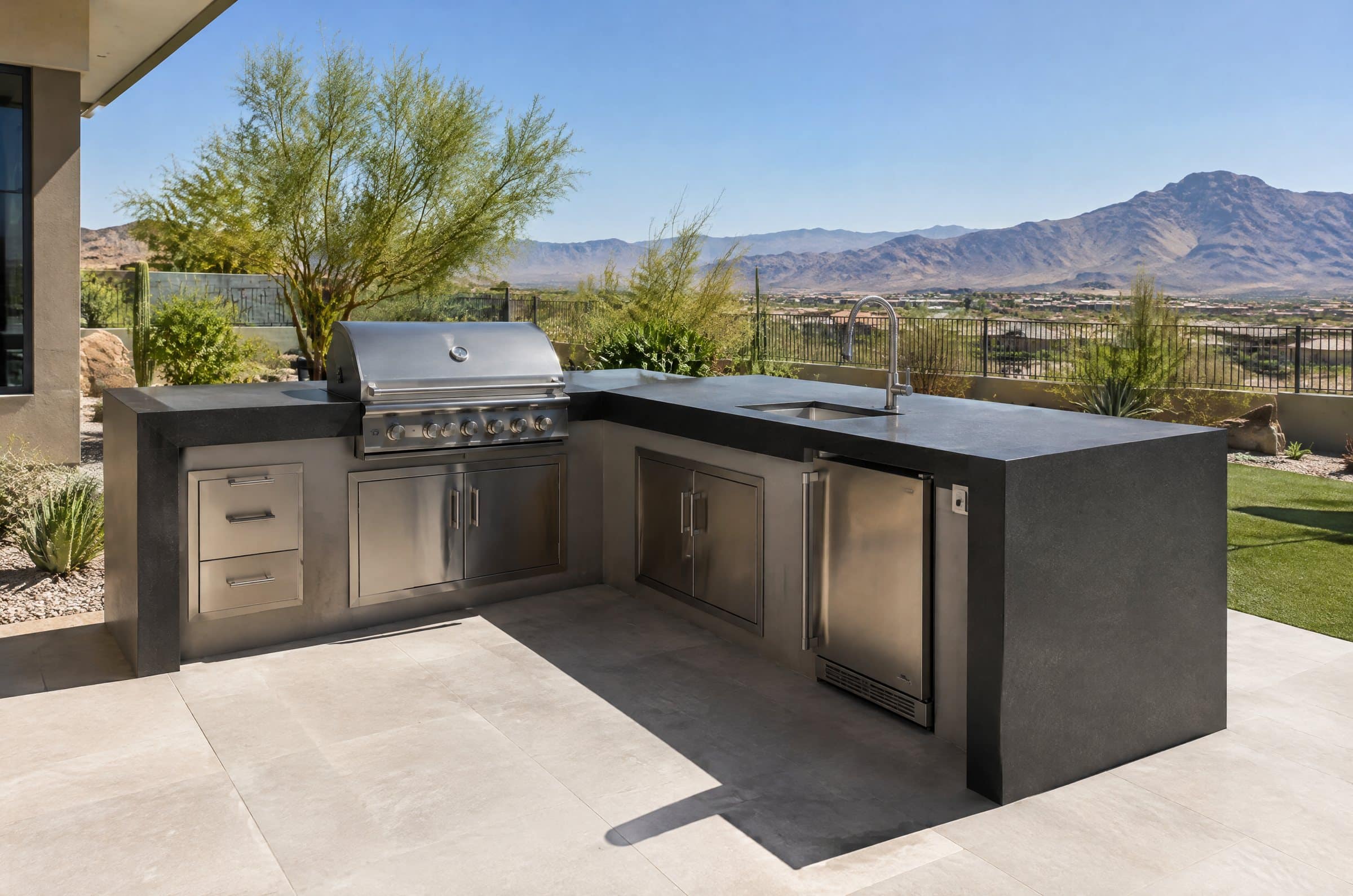 Outdoor kitchen with a matte charcoal ultra-compact countertop and built-in grill in full sun, desert mountains beyond